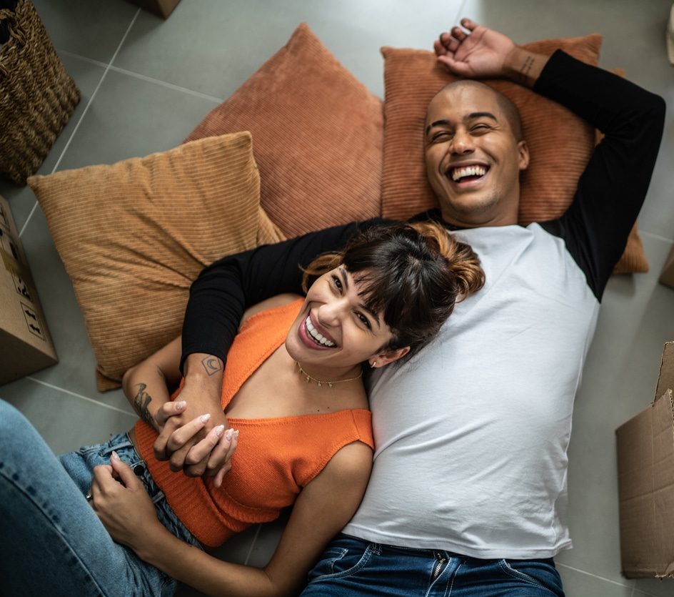Happy couple laughing and relaxing on pillows amid moving boxes, enjoying their new home.